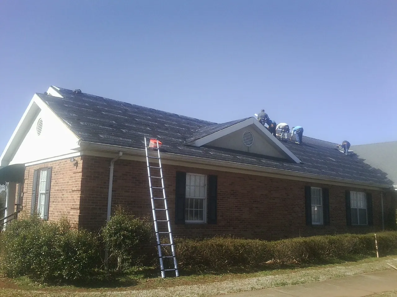 Crew tearing shingles off a brick ranch roof with a ladder set — Metal Roof Repair work by our crew in Belfast