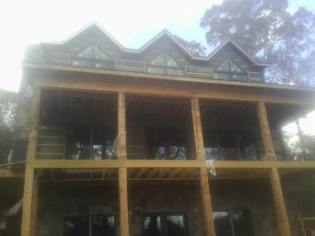 Dormers and porch framing on a large log home under construction — Roof Coating work by our crew in Belfast