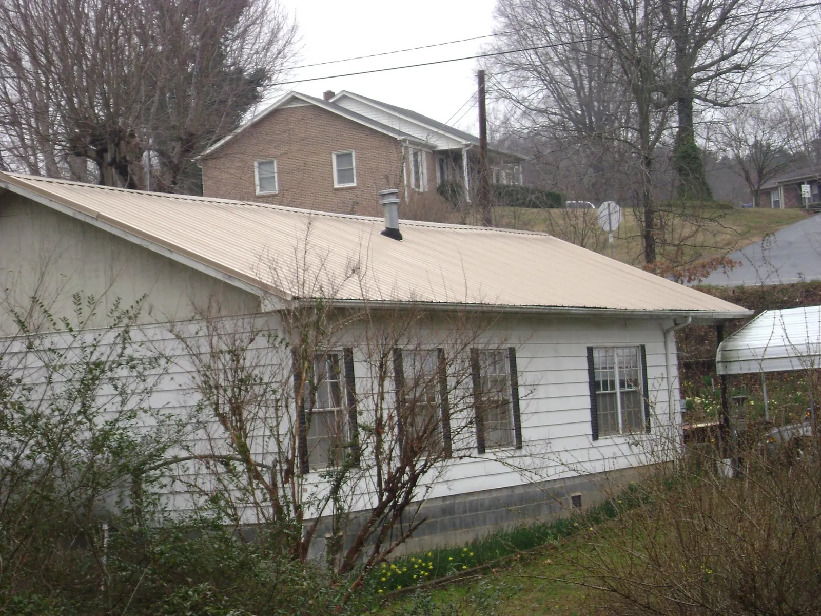 Tan metal roof on a white sided house set into a hillside — Commercial Roofing by Roofing Brothers in Belfast