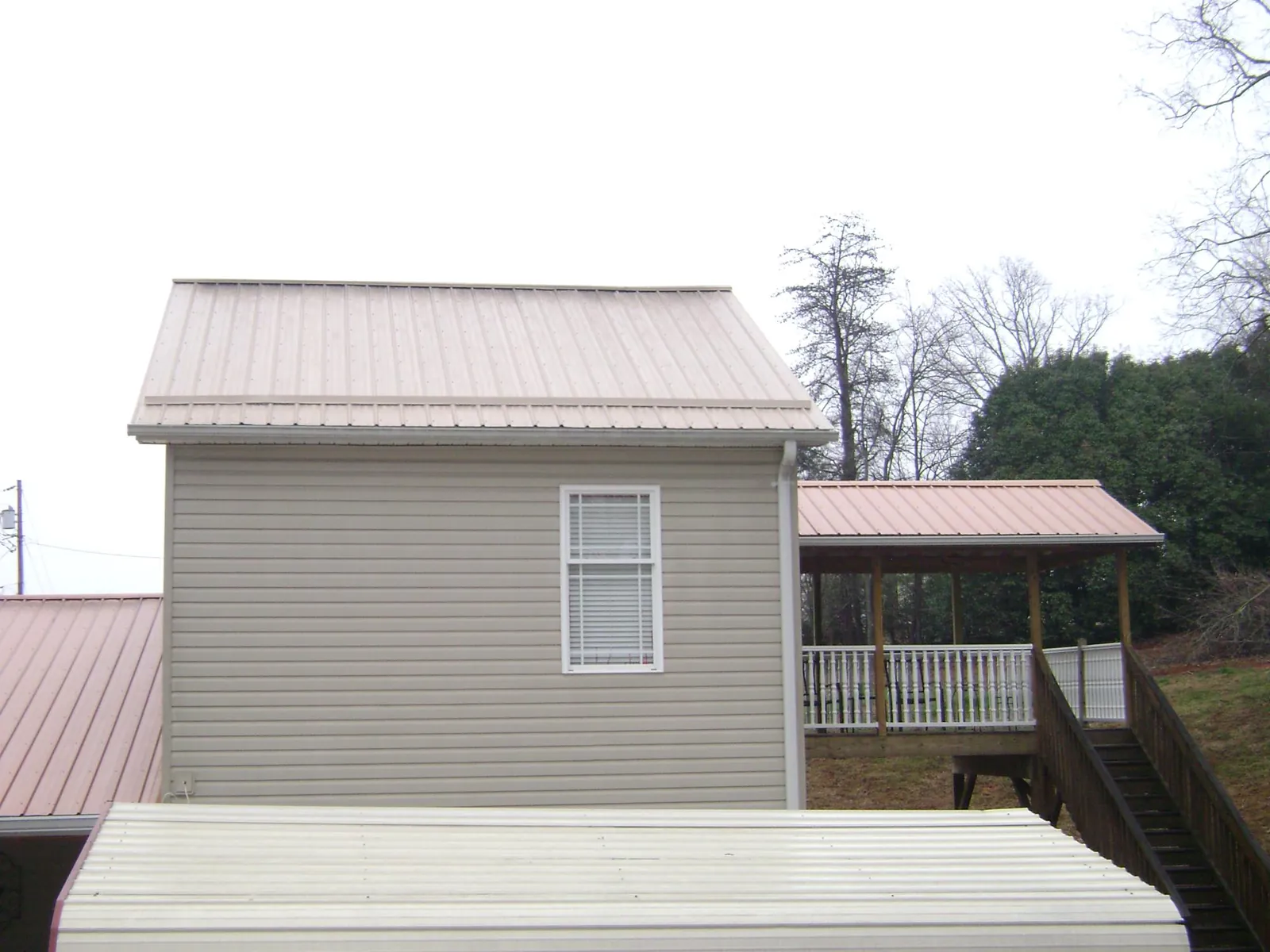Tan metal roofs on a two story addition and attached porch, from a Roof Replacement job in Belfast